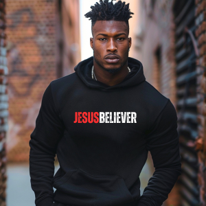 Person wearing a black hoodie with 'JESUS BELIEVER' text against a brick wall background